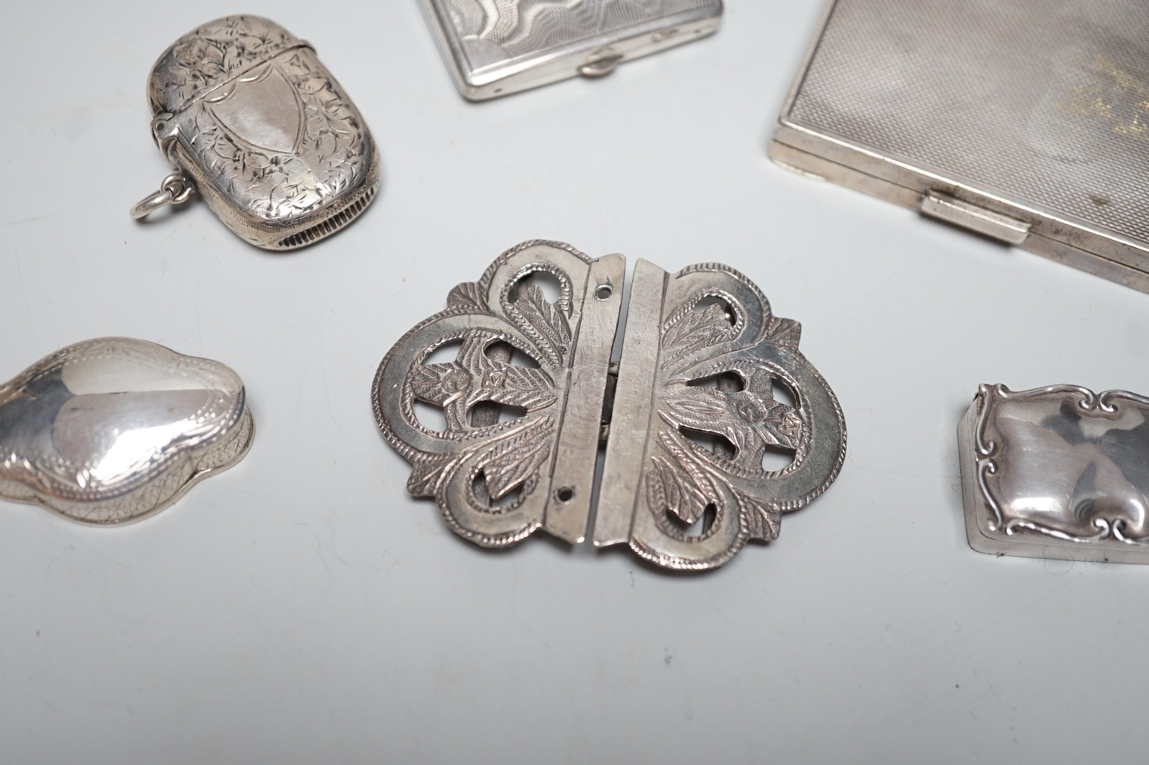 A George VI engine turned silver compact, 69mm, two modern silver pill boxes, a Persian white metal belt buckle, a silver vesta case and a base metal compact.